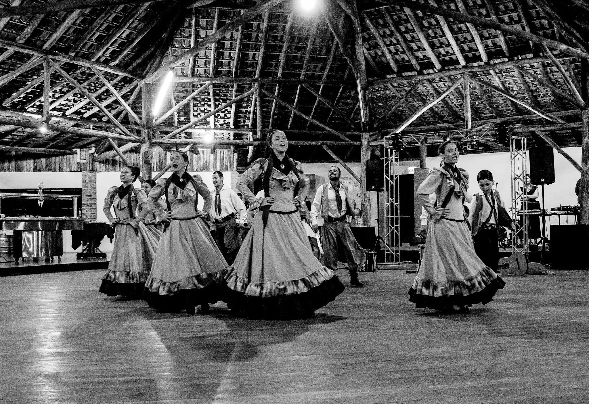 Black and white image of a cultural dance performance in a rustic indoor setting.