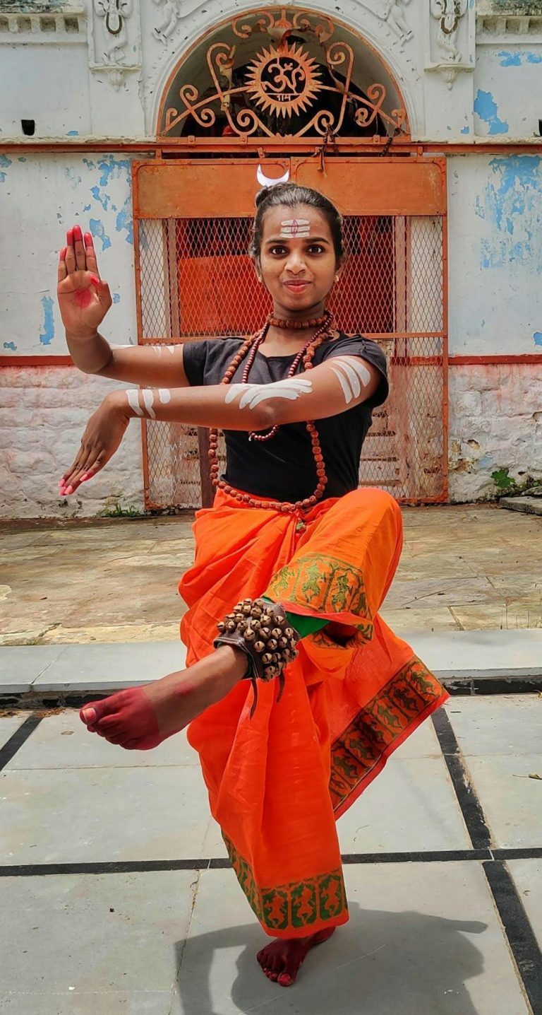 Woman performing traditional Indian dance in ornate orange sari, showcasing cultural elegance.