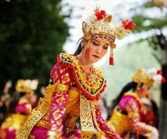 An enchanting Balinese dancer performing in vibrant traditional attire with others, creating a cultural spectacle outdoors.