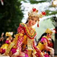 An enchanting Balinese dancer performing in vibrant traditional attire with others, creating a cultural spectacle outdoors.