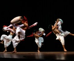 Dynamic group of dancers performing a traditional dance with drums on stage.
