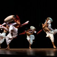 Dynamic group of dancers performing a traditional dance with drums on stage.
