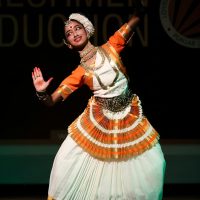 Smiling woman performing traditional Indian dance on stage in vibrant costume.