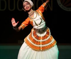 Smiling woman performing traditional Indian dance on stage in vibrant costume.