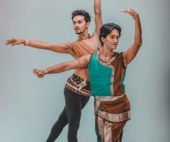 Two male dancers in traditional attire performing an elegant dance indoors.