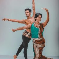 Two male dancers in traditional attire performing an elegant dance indoors.