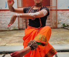 Woman performing traditional Indian dance in ornate orange sari, showcasing cultural elegance.