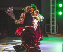 Women performing traditional dance on stage with colorful costumes and dynamic lighting.