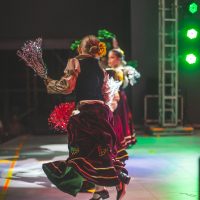 Women performing traditional dance on stage with colorful costumes and dynamic lighting.